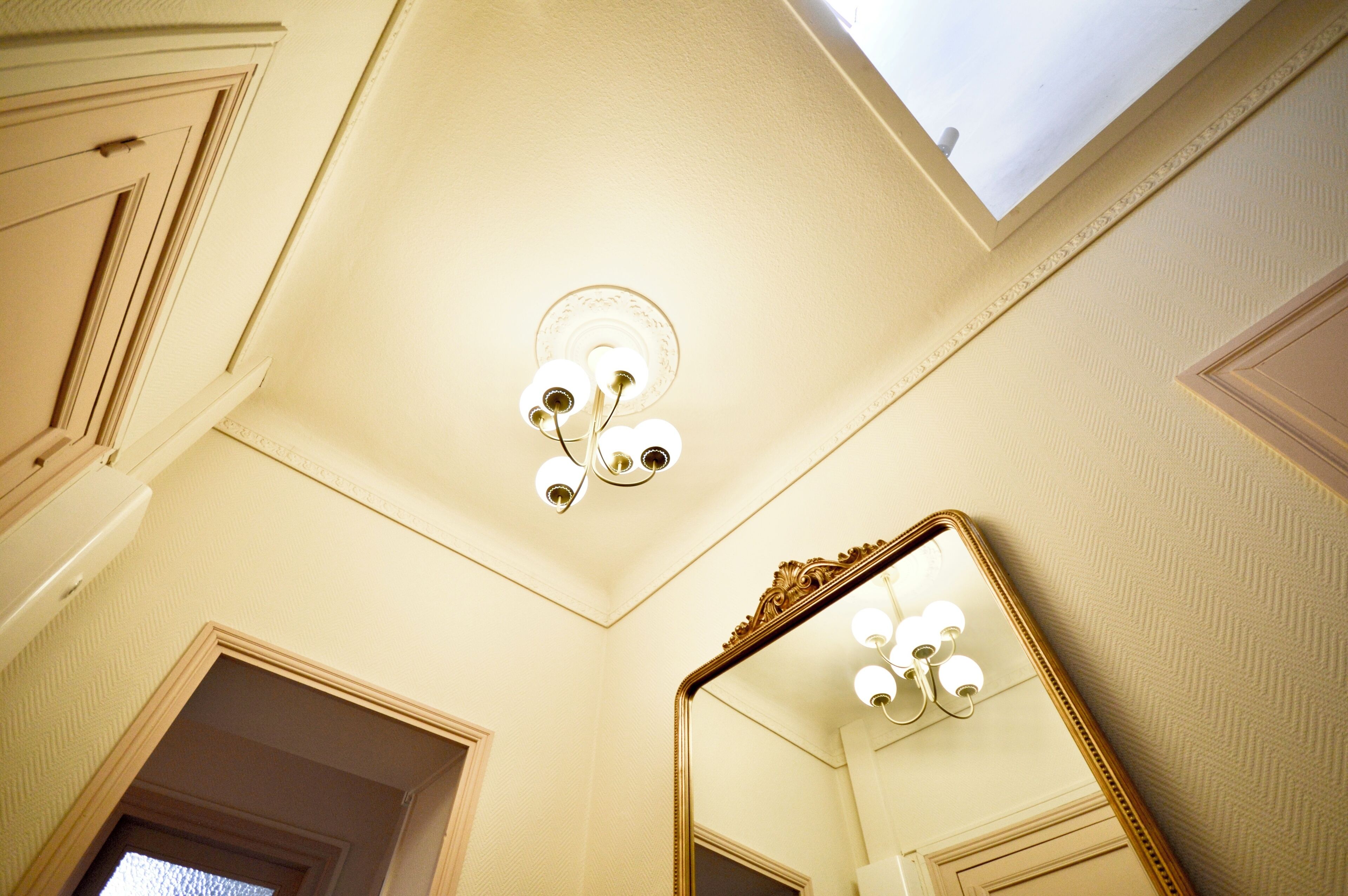 Une pièce avec un plafond haut, un lustre et un grand miroir.
