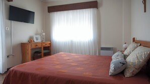 A bedroom with a bed, a desk, a chair, a television, and a window with curtains. - Apartamentos Turísticos Céu Azul (Vila Nova de Gaia)