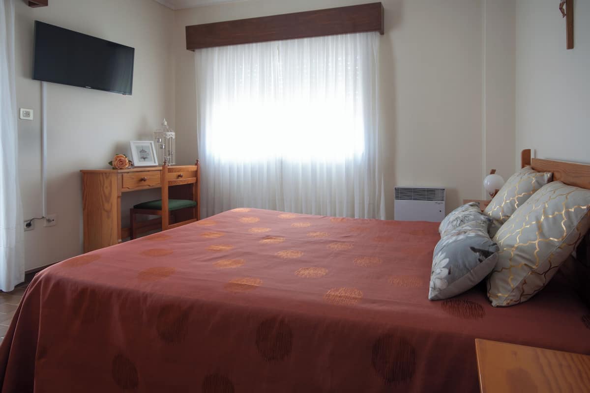 Un dormitorio con cama, escritorio, silla, televisión y ventana con cortinas.