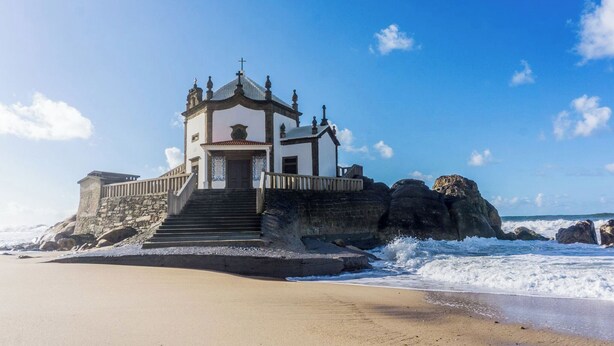 A coastal building with a staircase leading to a door, surrounded by rocky terrain and the sea. - Apartamentos Turísticos Céu Azul (Vila Nova de Gaia)