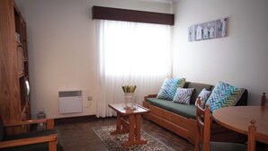 A living room with a sofa, wooden furniture, a small table with a vase, and a wall-mounted artwork. - Apartamentos Turísticos Céu Azul (Vila Nova de Gaia)