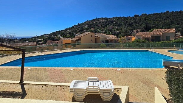Une piscine entourée de chaises longues, avec des maisons et un paysage vallonné tout autour.