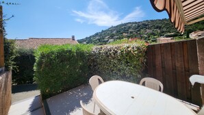 Une terrasse avec une table et des chaises, entourée de verdure et d’une clôture en bois.
