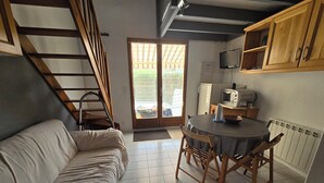 Un espace de vie compact comprenant un canapé, une table à manger avec des chaises, un coin cuisine avec un four à micro-ondes et un escalier.