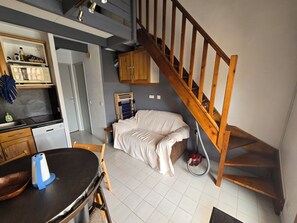 A compact living space with a kitchen area, a dining table, a sofa, and a wooden staircase.