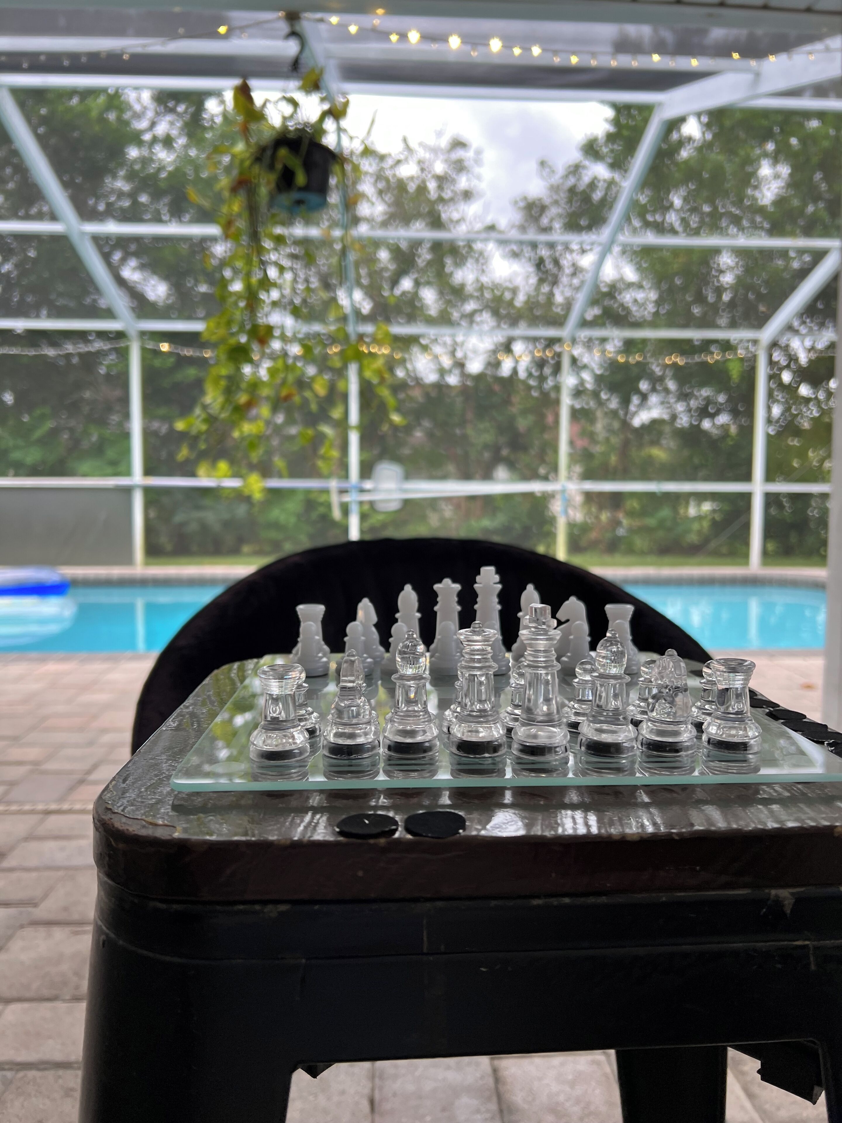 Un échiquier posé sur une table en verre, avec une piscine en arrière-plan.