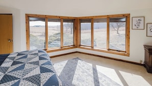 Ein Schlafzimmer mit großem Fenster, einem Bett mit gemustertem Überwurf und einem kleinen Wandbild.