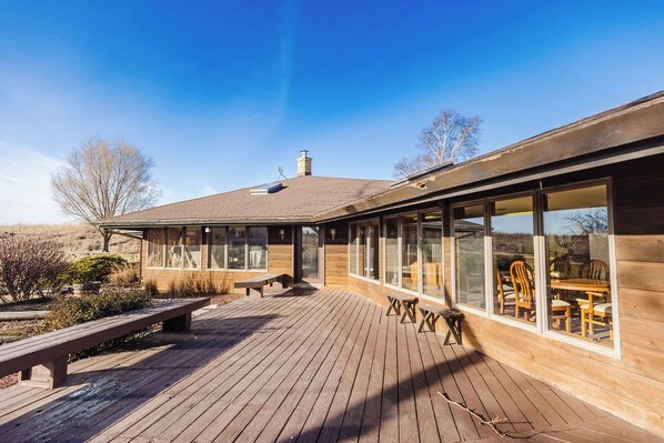 A wooden deck with a bench and a table, overlooking a landscape with trees and a clear sky.