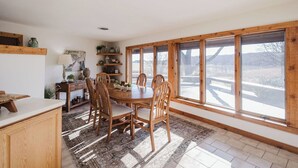 Ein Essbereich mit einem Holztisch, Stühlen, einem Teppich und Blick auf eine verschneite Landschaft durch große Fenster.