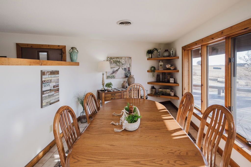 Een eetkamer met een houten tafel, stoelen, een decoratief middelpunt en planken met planten en decoratieve objecten.