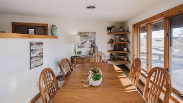 Een eetkamer met een houten tafel, stoelen, een decoratief middelpunt en planken met planten en decoratieve objecten.