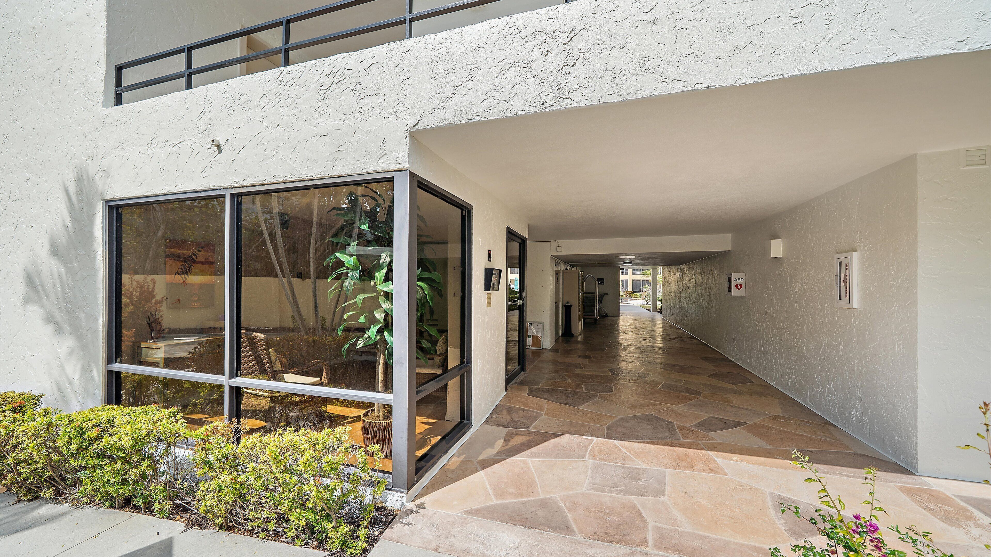 A modern building with a glass entrance, a stone-tiled hallway, and an outdoor seating area with plants.