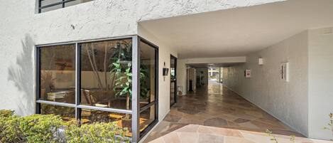 A modern building with a glass entrance, a stone-tiled hallway, and an outdoor seating area with plants.