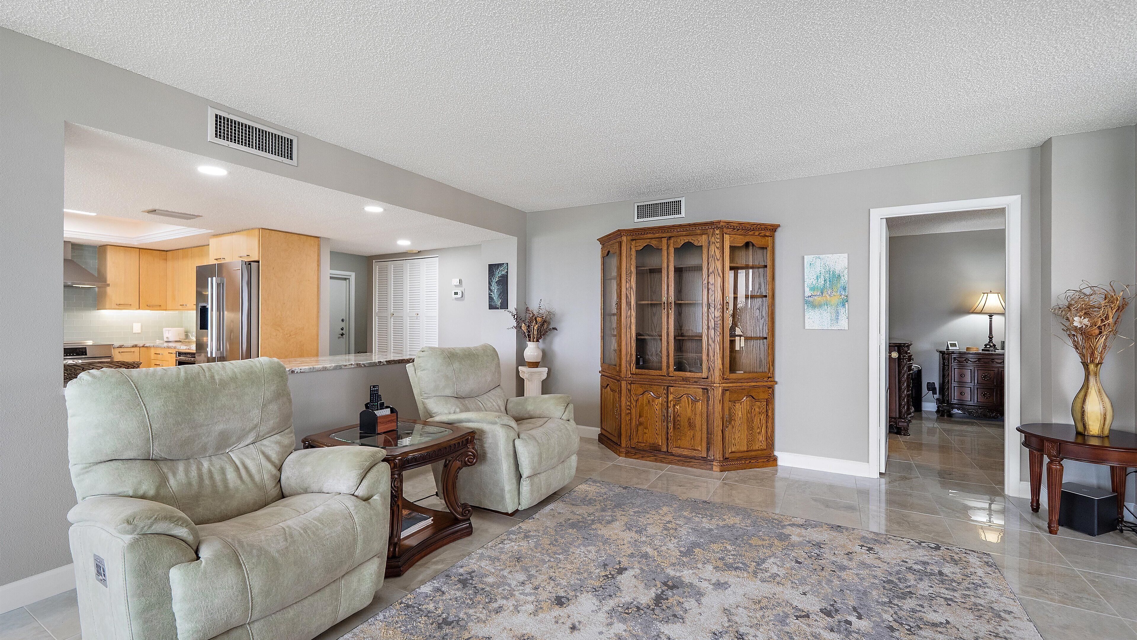 A spacious living room with a large wooden cabinet, two armchairs, and a coffee table.