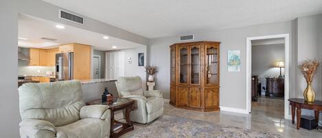 A spacious living room with a large wooden cabinet, two armchairs, and a coffee table.