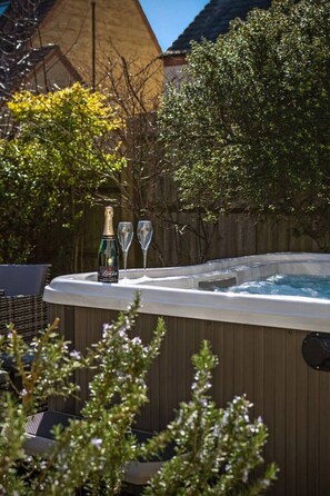 Un bain à remous avec une bouteille et deux verres posés sur le bord, entouré de verdure.