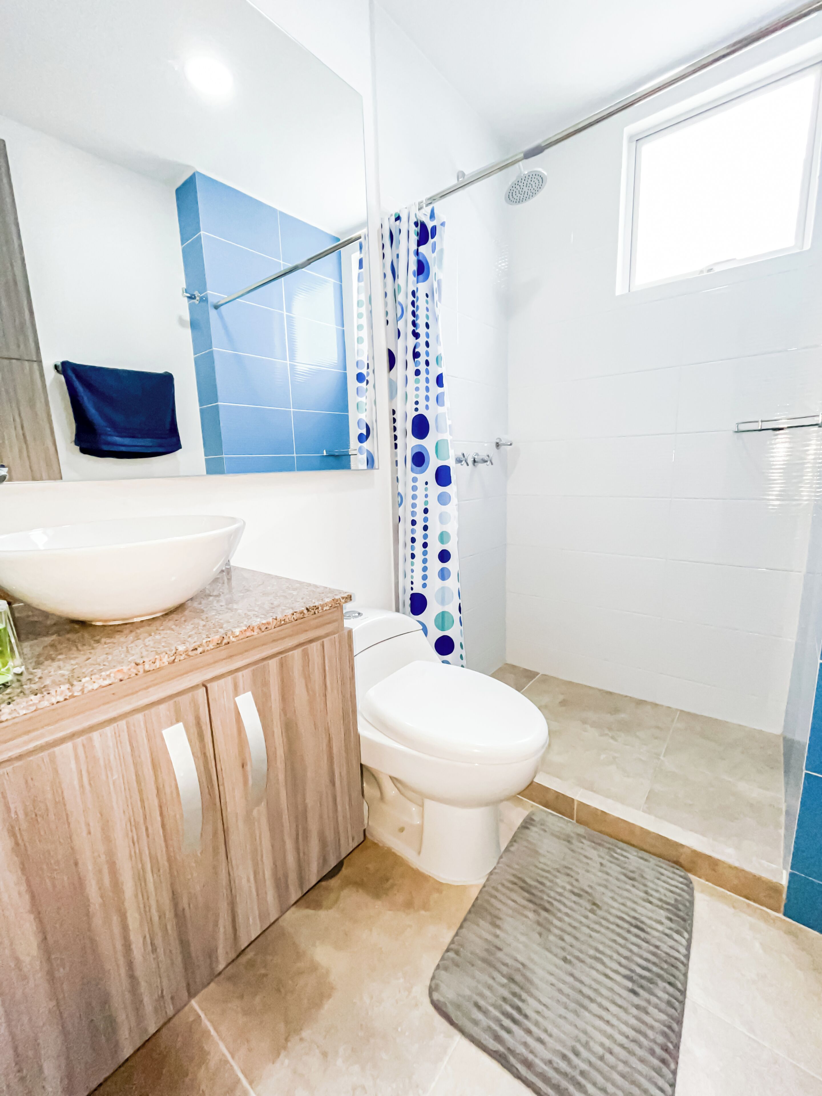 Un baño con un lavabo grande blanco, un inodoro, una ducha con cortina celeste y blanca a lunares, y un espejo sobre el lavabo.