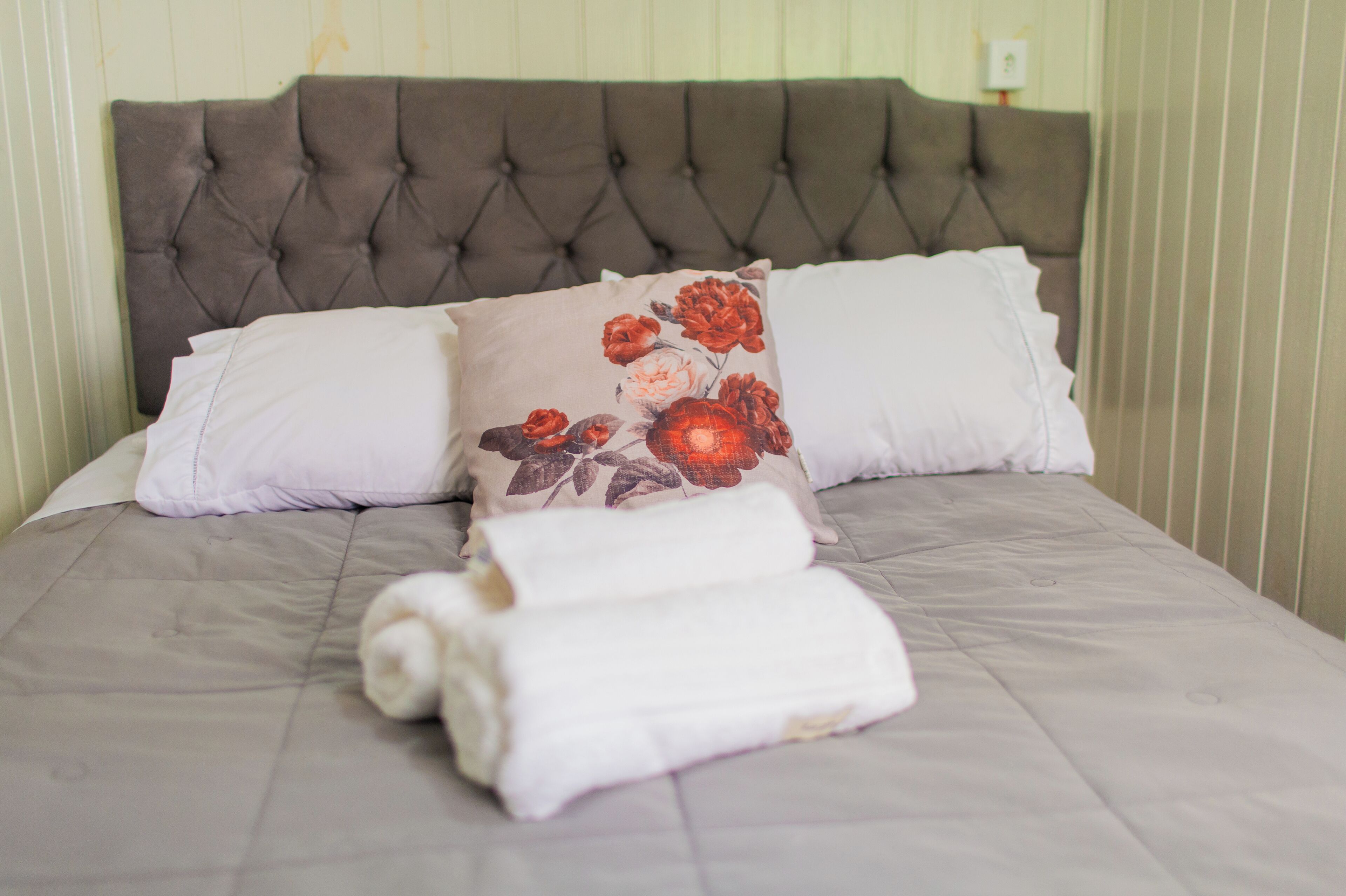 A neatly made bed with a tufted headboard, two pillows, and rolled towels.