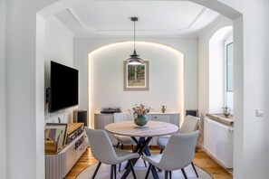 A modern dining area with a round table, chairs, a television, and a ceiling light fixture. - Apartment 'Schwarzmühle 2' with Lake View, Private Garden and Wi-Fi (Börnichen/Erzgeb.)