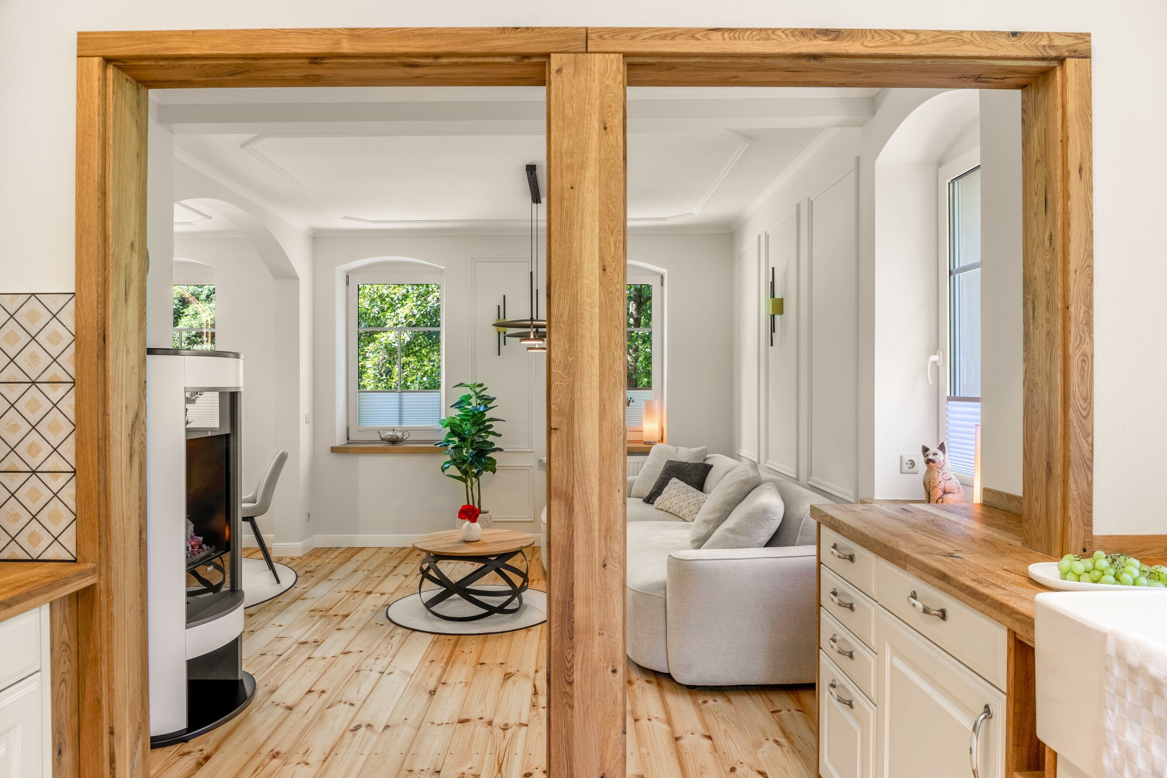 A modern interior with a wooden floor, a dining area with a round table, a sofa, and a kitchen area with cabinets and a countertop.