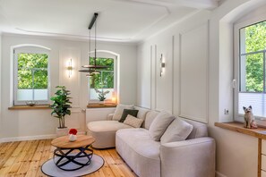 A modern living room with a beige sofa, a wooden coffee table, and a potted plant. - Apartment 'Schwarzmühle 2' with Lake View, Private Garden and Wi-Fi (Börnichen/Erzgeb.)