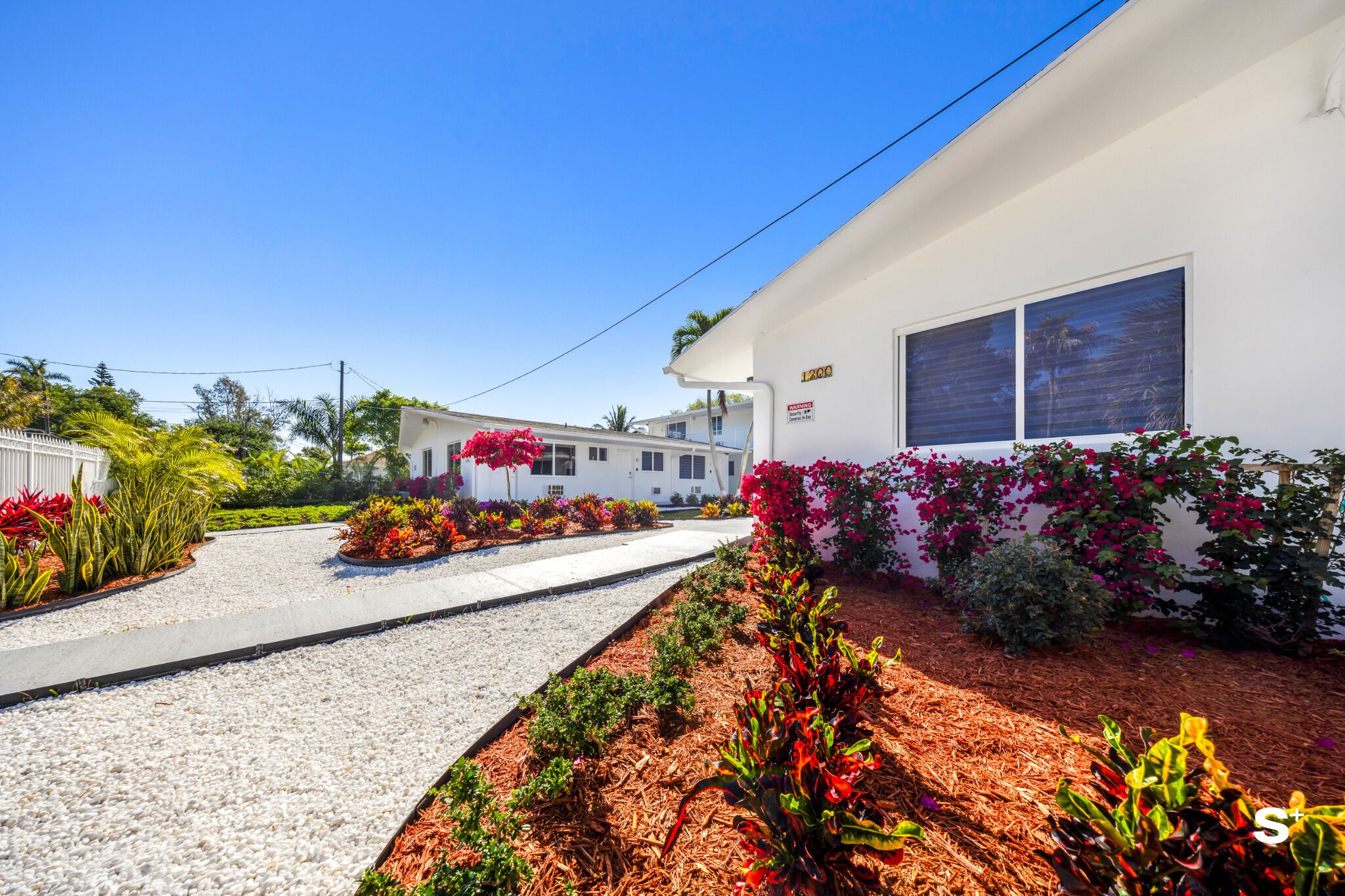 A white building with a gravel driveway and flower beds.