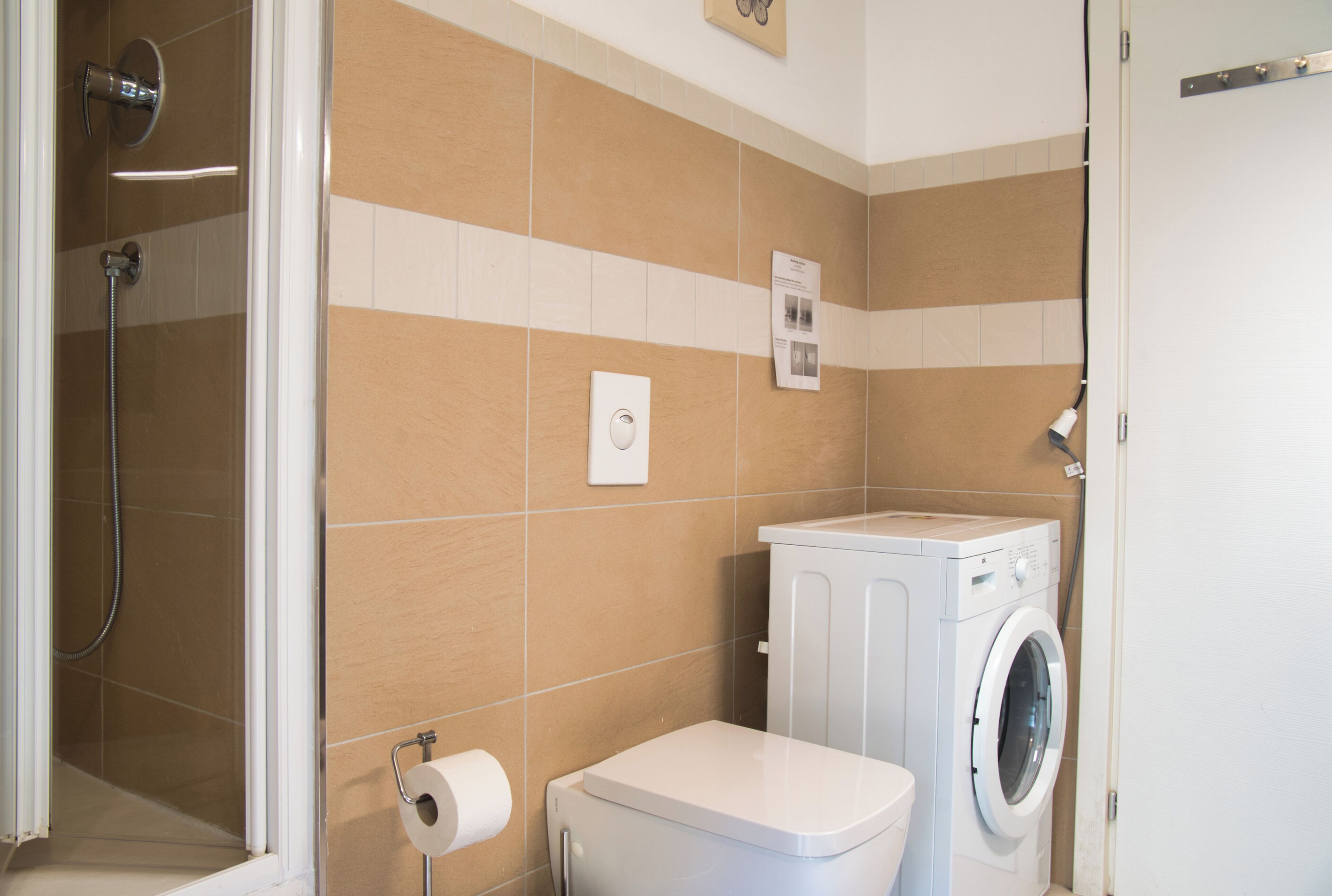 Une salle de bain équipée d’une douche, de toilettes et d’un lave-linge.