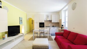 A compact living space with a TV, sofa, dining table, chairs, kitchen area, and a red couch. - Casa Rosa - hidden Garden with lake view (Fiumelatte)