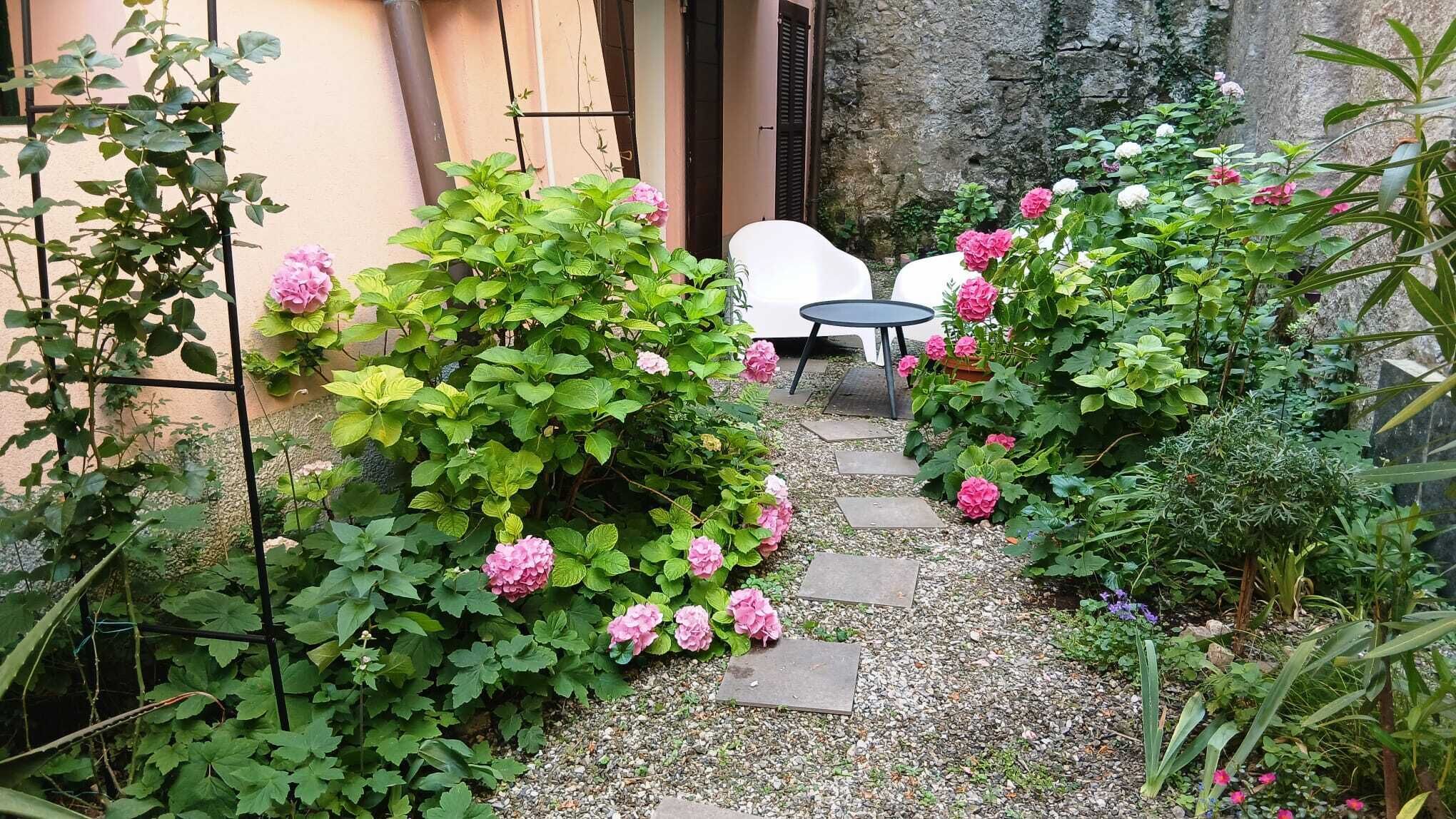 Un jardín con un sendero de grava, una silla blanca y una mesa.