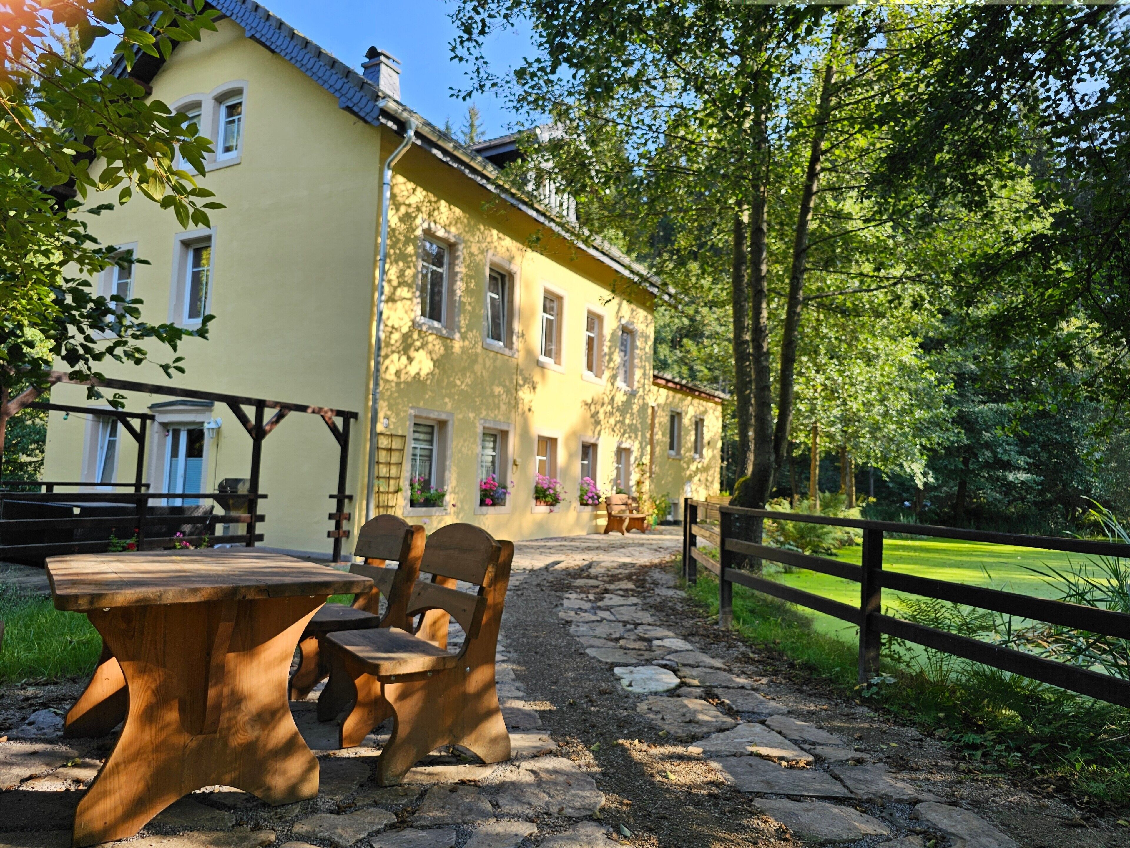 Un bâtiment jaune avec un chemin de pierre menant à un banc et une table en bois.