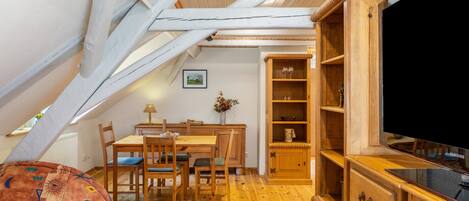 Acogedor dormitorio en ático con una mesa de comedor de madera, sillas, un televisor y una estantería.