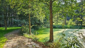 Ein gepflasterter Weg führt durch einen üppigen Garten mit Bäumen und Pflanzen.