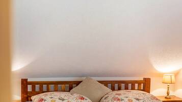 Ein Bett mit floralem Bettbezug und einem Holz-Kopfteil, eine Nachttischlampe und eine schlichte Wand.