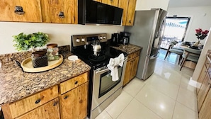 A modern kitchen with wooden cabinets, stainless steel appliances, granite countertops, and a central island with a kettle. - Pool+Spa+ 3.5 Baths+Outdoor Grill (Bradenton)