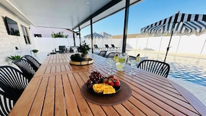 A wooden table with a fruit platter, surrounded by black and white striped chairs, under a striped umbrella. - Pool+Spa+ 3.5 Baths+Outdoor Grill (Bradenton)