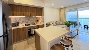 A modern kitchen with a central island, wooden cabinets, and a view of the sea through large windows. - Ocean view loft, Harbor 171 (Puerto Vallarta)