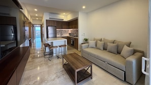 A modern living room with a sofa, a coffee table, and a TV. There is a kitchen area with cabinets and a refrigerator. - Ocean view loft, Harbor 171 (Puerto Vallarta)
