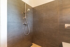 Une douche équipée d’un pommeau de douche à main et d’un robinet mural, ainsi qu’un sol carrelé et des toilettes situées dans un coin.
