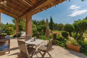 Une terrasse extérieure avec une table et des chaises, entourée de plantes en pot et agrémentée d’une pergola.