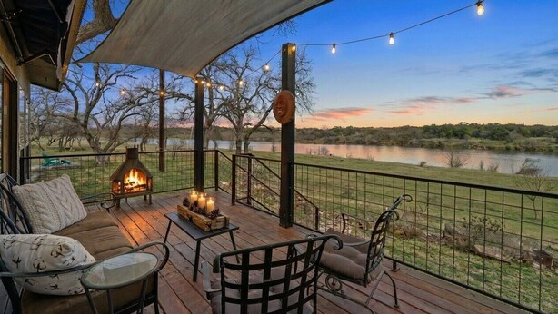 Une terrasse avec coin salon extérieur, un foyer et vue sur un lac.