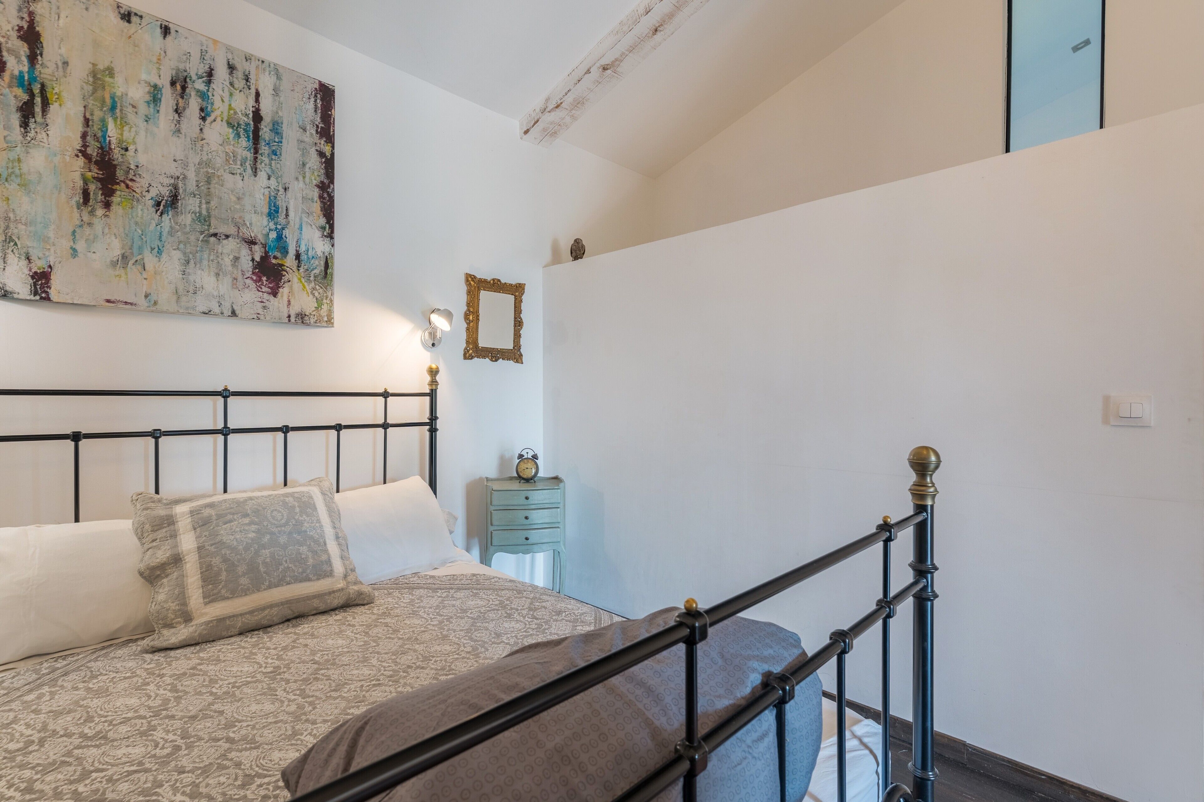 A bedroom with a bed, a nightstand, a wall clock, and a large abstract painting.