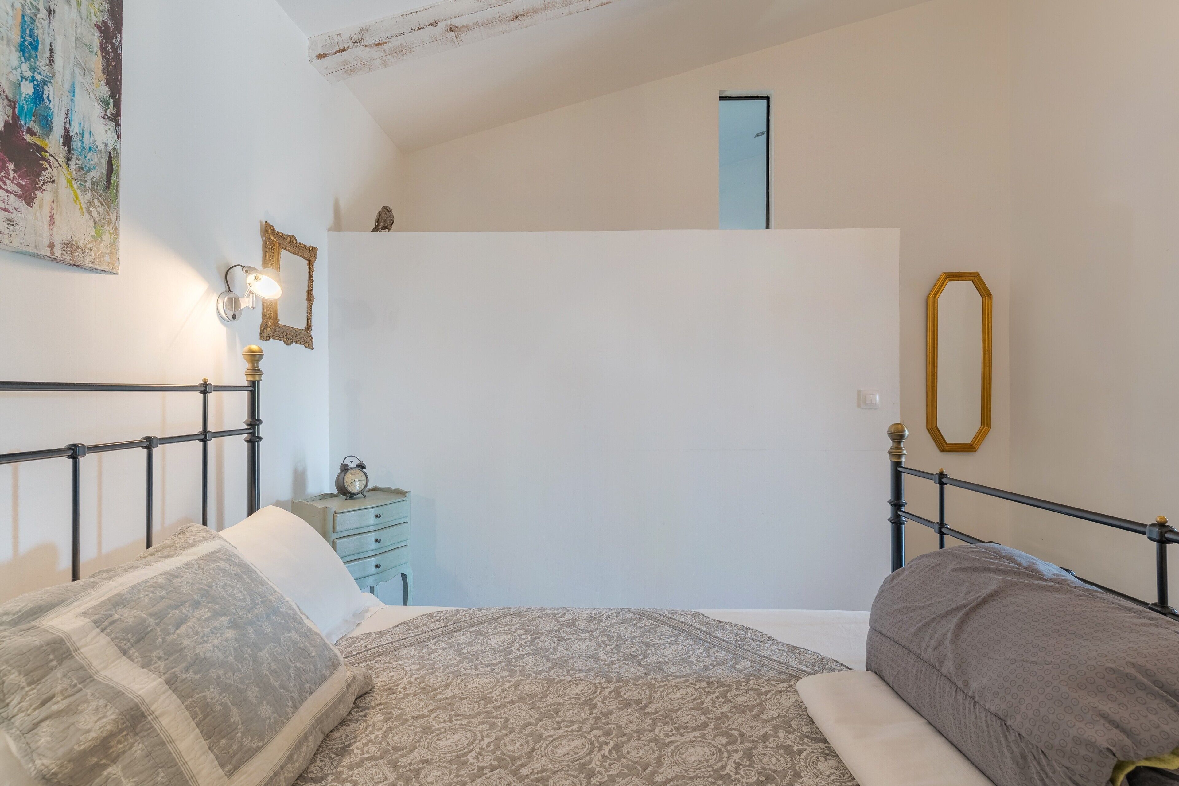 Ein Schlafzimmer mit Bett, Nachttischen, einem Spiegel an der Wand und einer Tür.