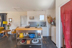 Una cocina compacta con una isla central, un área de comedor con una silla amarilla y una cortina roja.