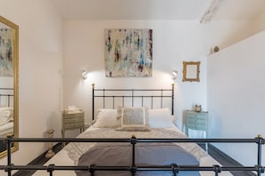 A bedroom with a bed, bedside tables, a mirror, and a wall art piece.
