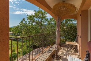 A balcony with a metal railing, a wicker basket, a folding chair, and a view of greenery and distant hills. - Holiday Home 'Lacoste Home' with Mountain View, Shared Pool and Wi-Fi (Lacoste)