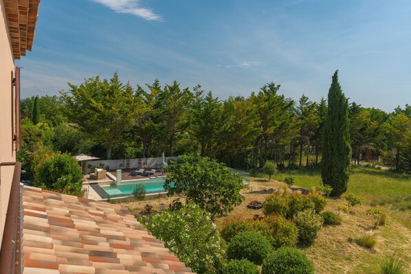 A residential area with a swimming pool, lush greenery, and a tiled roof.