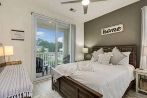 Une chambre avec un grand lit, une vue sur l’extérieur, un ventilateur de plafond et un panneau indiquant « chez soi » sur le mur.