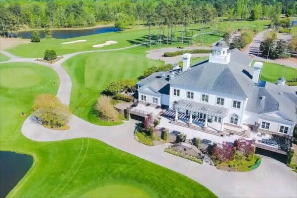 Une grande maison à deux étages, dotée d’un porche abrité, entourée d’un terrain de golf bien entretenu et d’un petit lac.