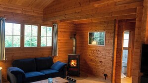 Interior d'una cabana de fusta amb un sofà, una llar de foc i una televisió.