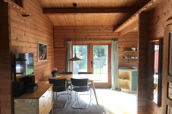 A wooden cabin interior with a dining table, chairs, a television, and a kitchen area. - Time out in a log cabin/holiday home - peace and relaxation not far from the beach in Grömitz (Grömitz)